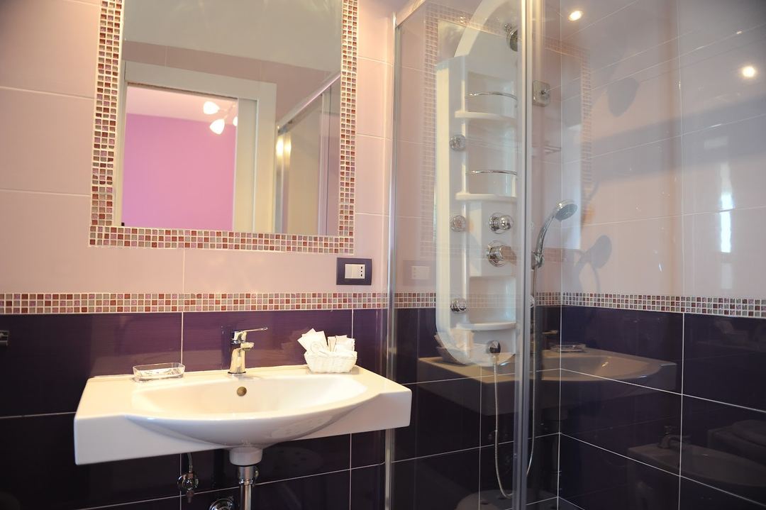 Modern bathroom featuring a curved white sink, dark tile accents with mosaic border trim, and a glass-enclosed shower with built-in shelving.